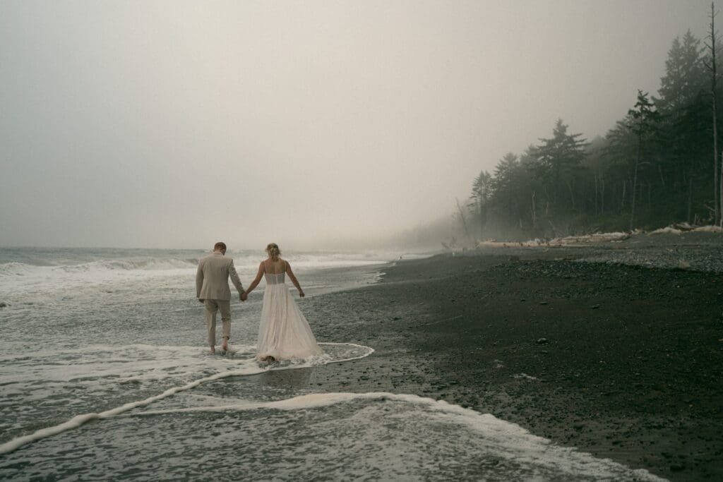 Couple walking along a foggy Oregon coast beach after their elopement ceremony