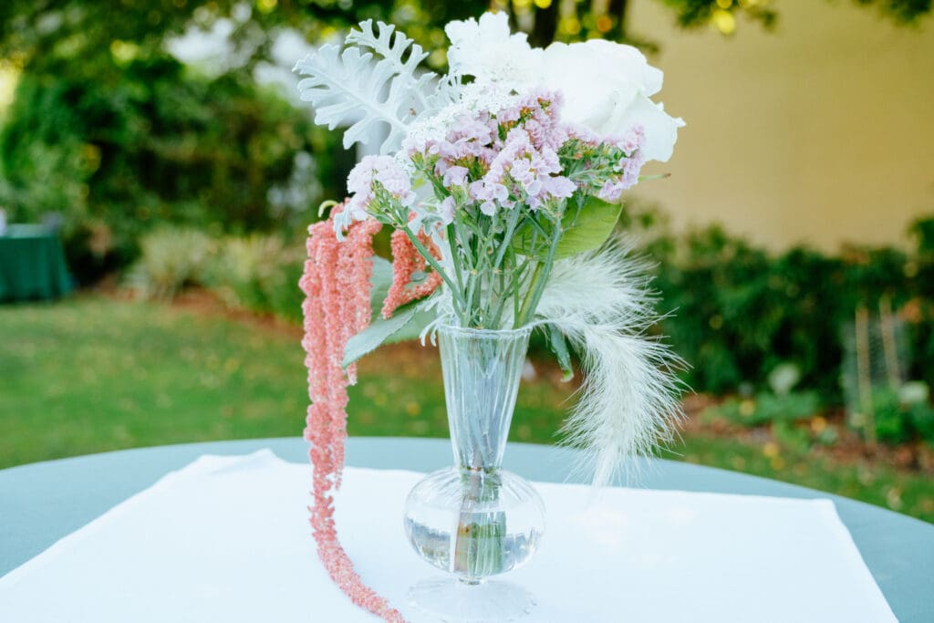 Small glass vase with pink and white flowers and greenery on a table outdoors