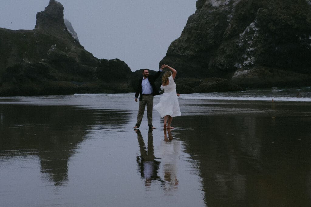 Groom twirling bride on reflective wet sand at Cannon Beach