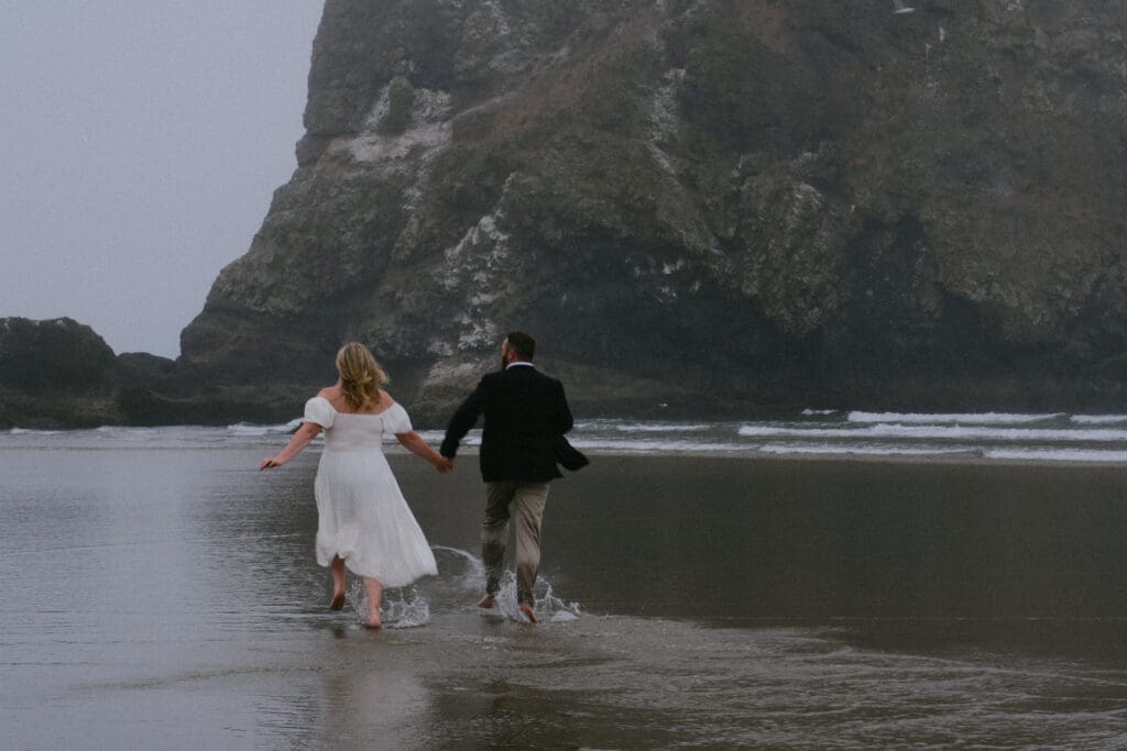 Couple walking along the shoreline at Cannon Beach during a foggy Oregon elopement