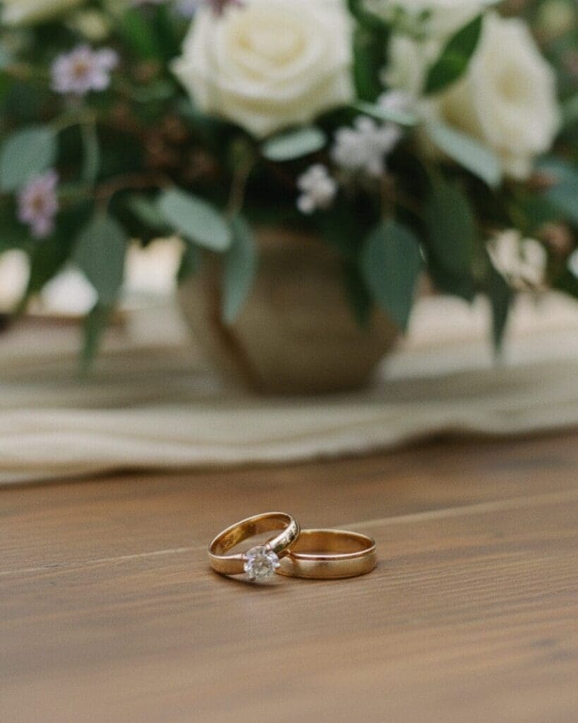 Close-up of wedding rings on a wooden table with soft floral background