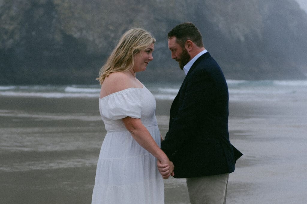 Couple holding hands during a misty Cannon Beach elopement with sea stacks in the background.
