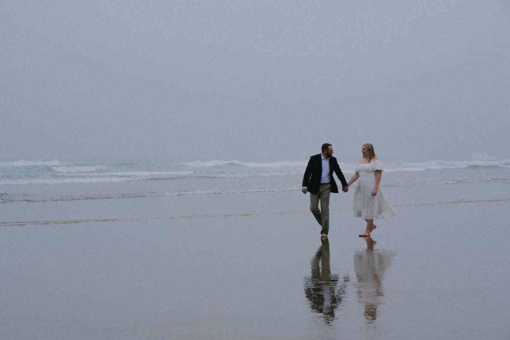 Bride and groom strolling along the waterline on a foggy Cannon Beach elopement day.