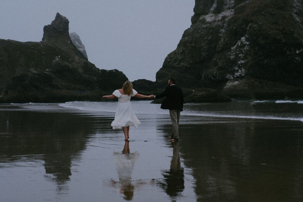 Couple embracing on the sand with coastal cliffs behind them at their Cannon Beach elopement.