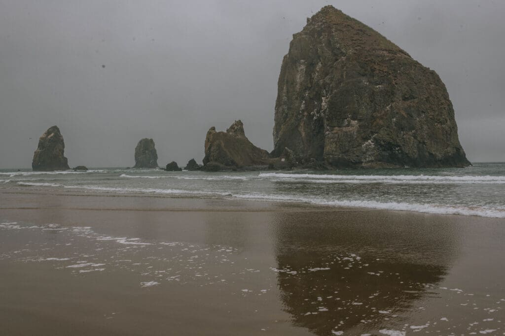 Foggy view of Haystack Rock and sea stacks at Cannon Beach on the Oregon Coast, a moody setting for a Cannon Beach elopement