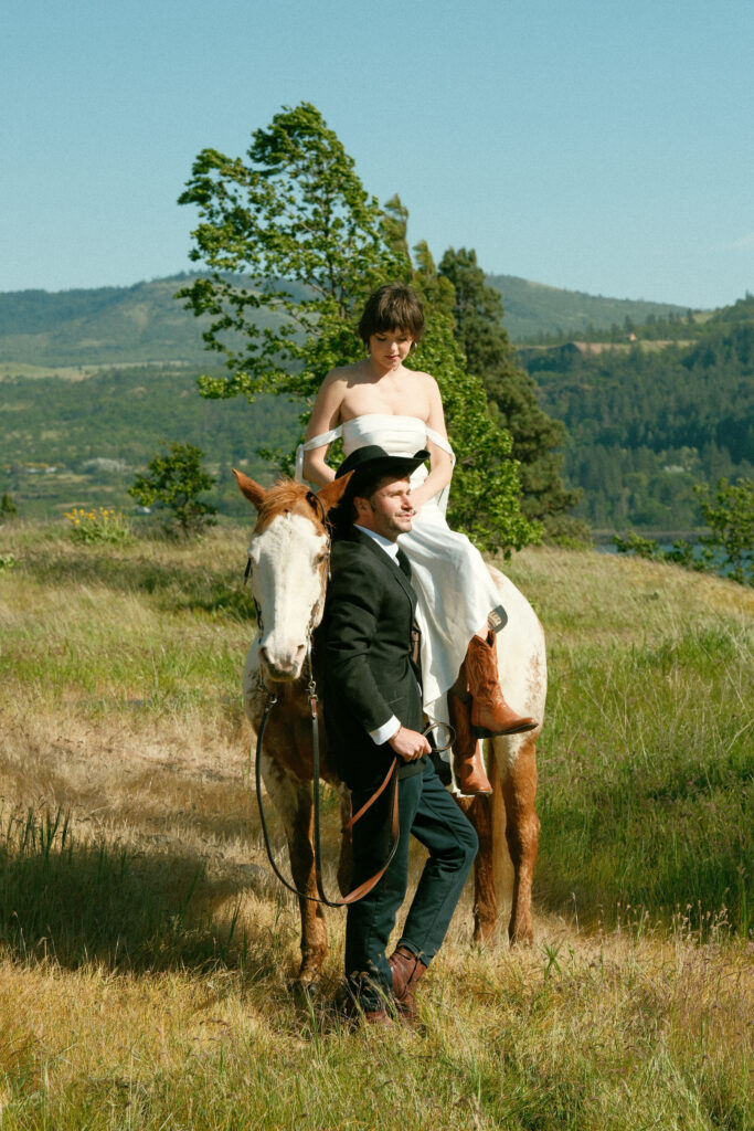 Columbia River Gorge elopement couple standing with their horse in a golden field with hills in the background


