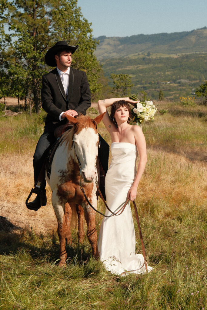 Cowboy‑hat groom on horseback with bride in a simple white gown holding a bouquet in the Columbia River Gorge

