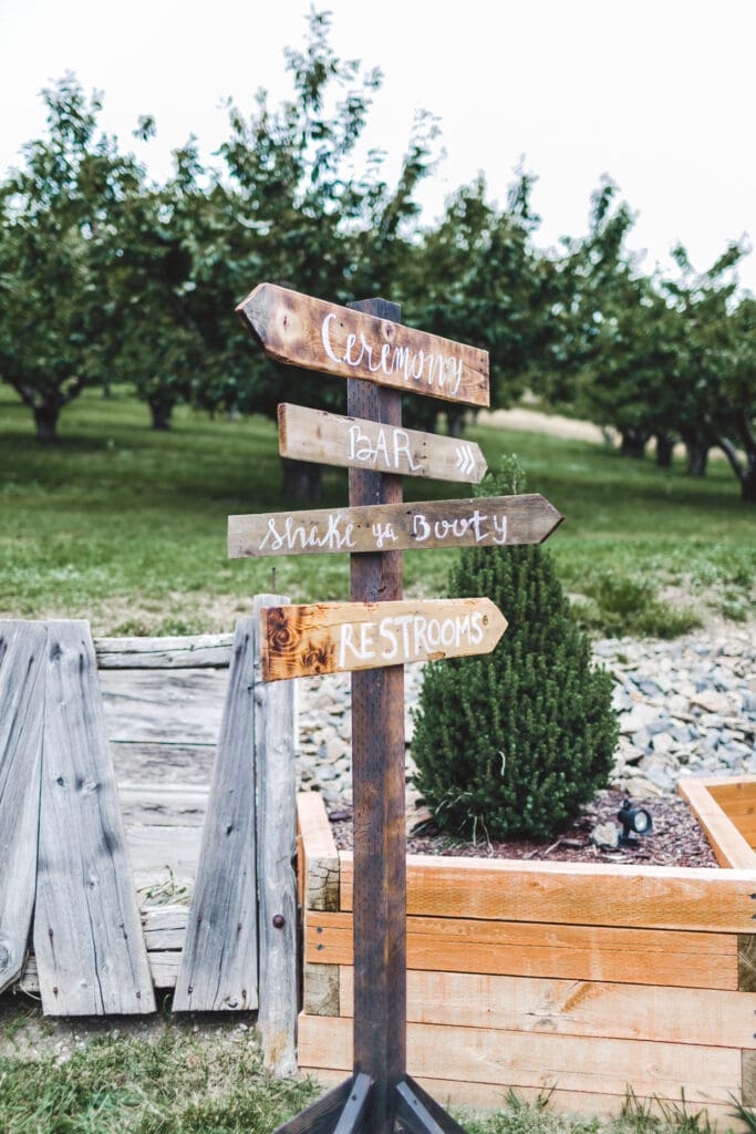 Simple wooden direction sign for ceremony and bar at an outdoor PNW elopement planned by a PNW wedding planner