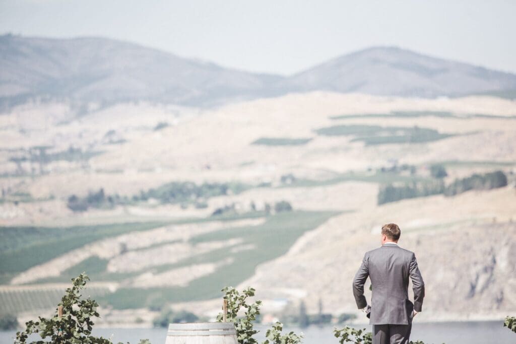 Groom in a suit standing by a lake with mountain views during a Pacific Northwest elopement