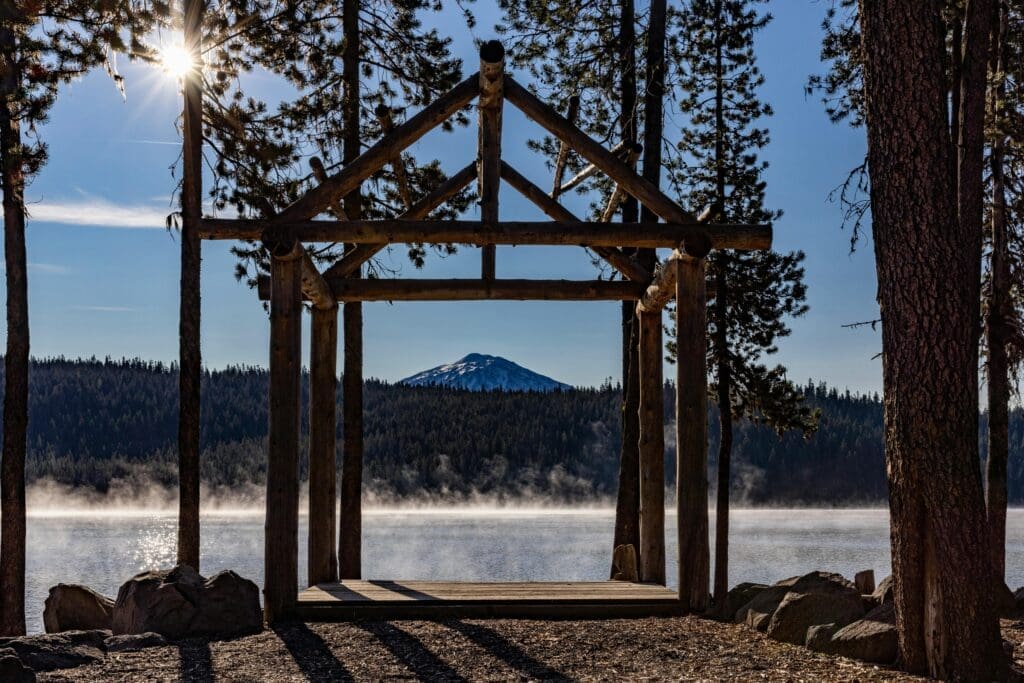Triangular wooden wedding arch with florals glowing in warm golden sunset light surrounded by Ponderosa pine trees near Bend Oregon