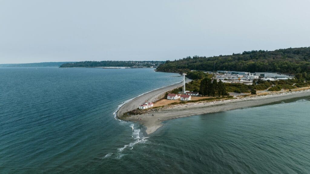 Aerial view of Seattle Puget Sound shoreline with a white lighthouse and forested coastline, a scenic Pacific Northwest wedding location