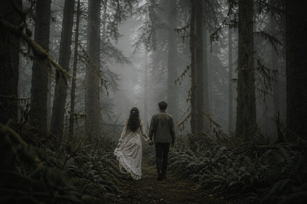 A couple walks hand in hand through the foggy Hoh Rain Forest in a Twilight-inspired Olympic National Park wedding scene surrounded by towering moss-covered trees and muted green tones.