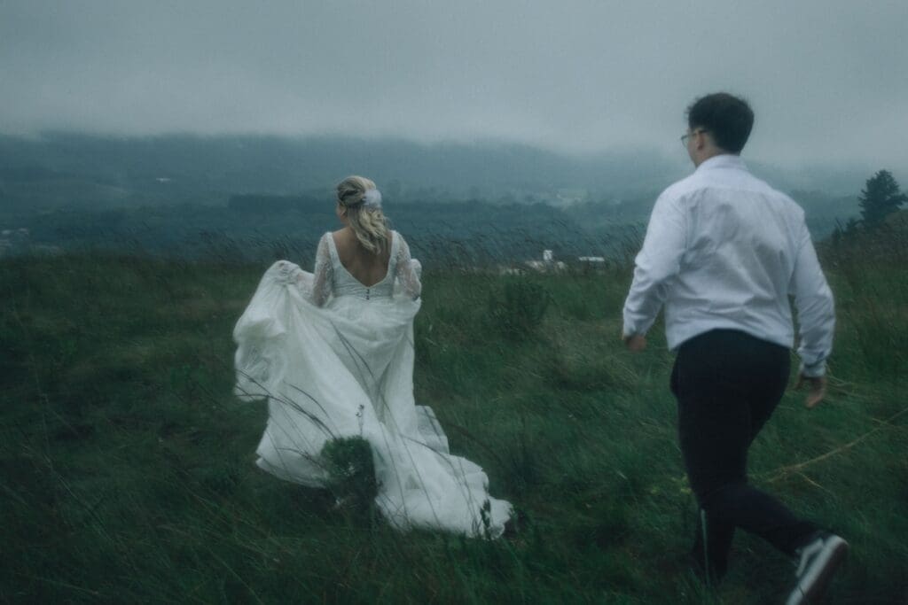 Couple walking through a misty field during a Pacific Northwest elopement, showing how fog and rain can become part of the experience.
