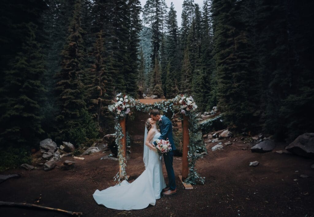 Bride and groom sharing a kiss beneath a floral arbor during a forest elopement ceremony near Eugene Oregon.