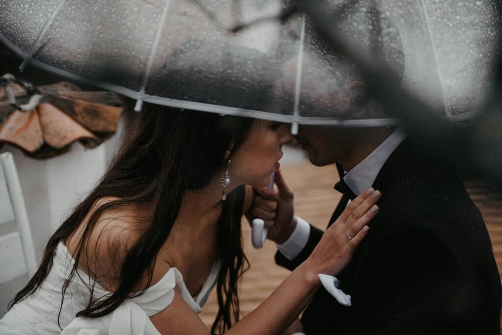 Couple sharing a quiet moment beneath a clear umbrella during a rainy outdoor wedding ceremony.