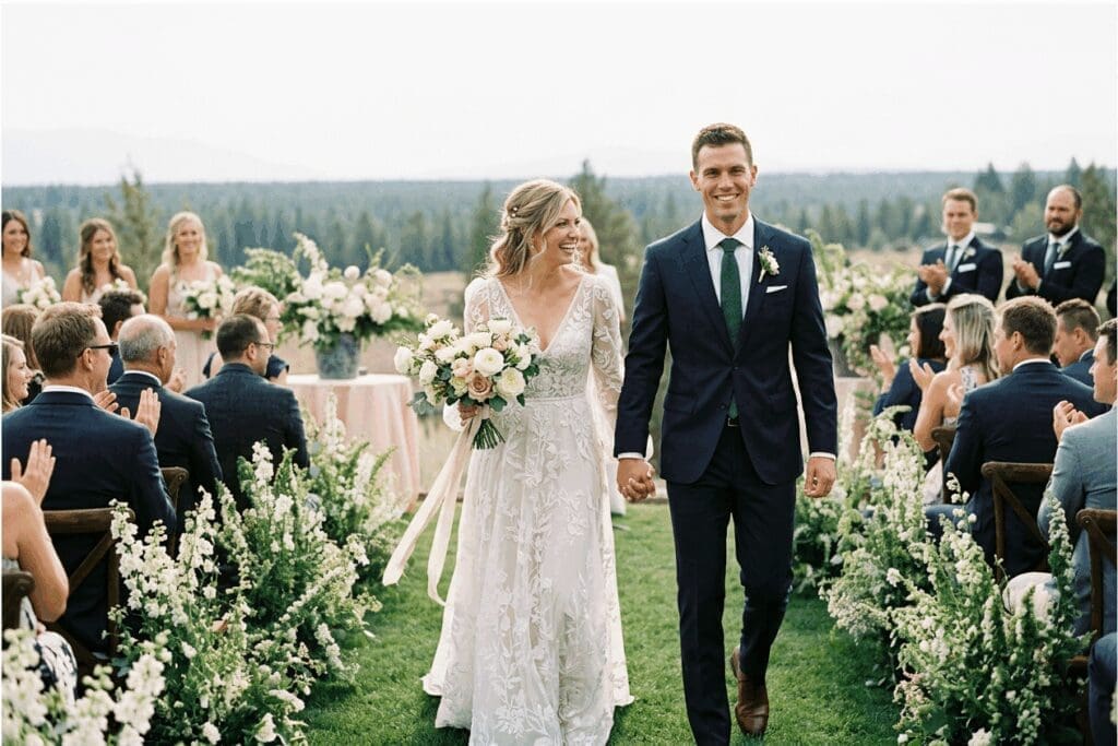 Outdoor Bend, Oregon micro wedding ceremony with a bride and groom walking down the aisle surrounded by guests and floral arrangements.