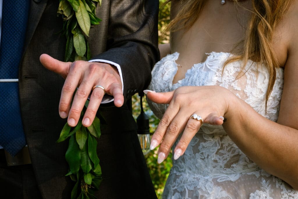Bride and groom show off their wedding rings, groom in a maile lei, at their Lake Oswego wedding

