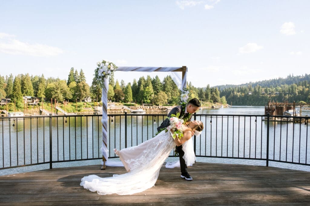 Groom dips the bride for a kiss under the floral arbor overlooking the river at The Foundry in Lake Oswego