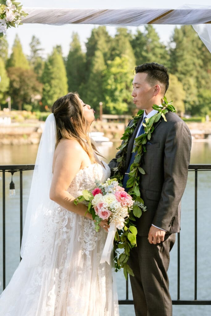 Groom wearing a maile lei facing his bride with her pink and white bouquet at an intimate Portland wedding