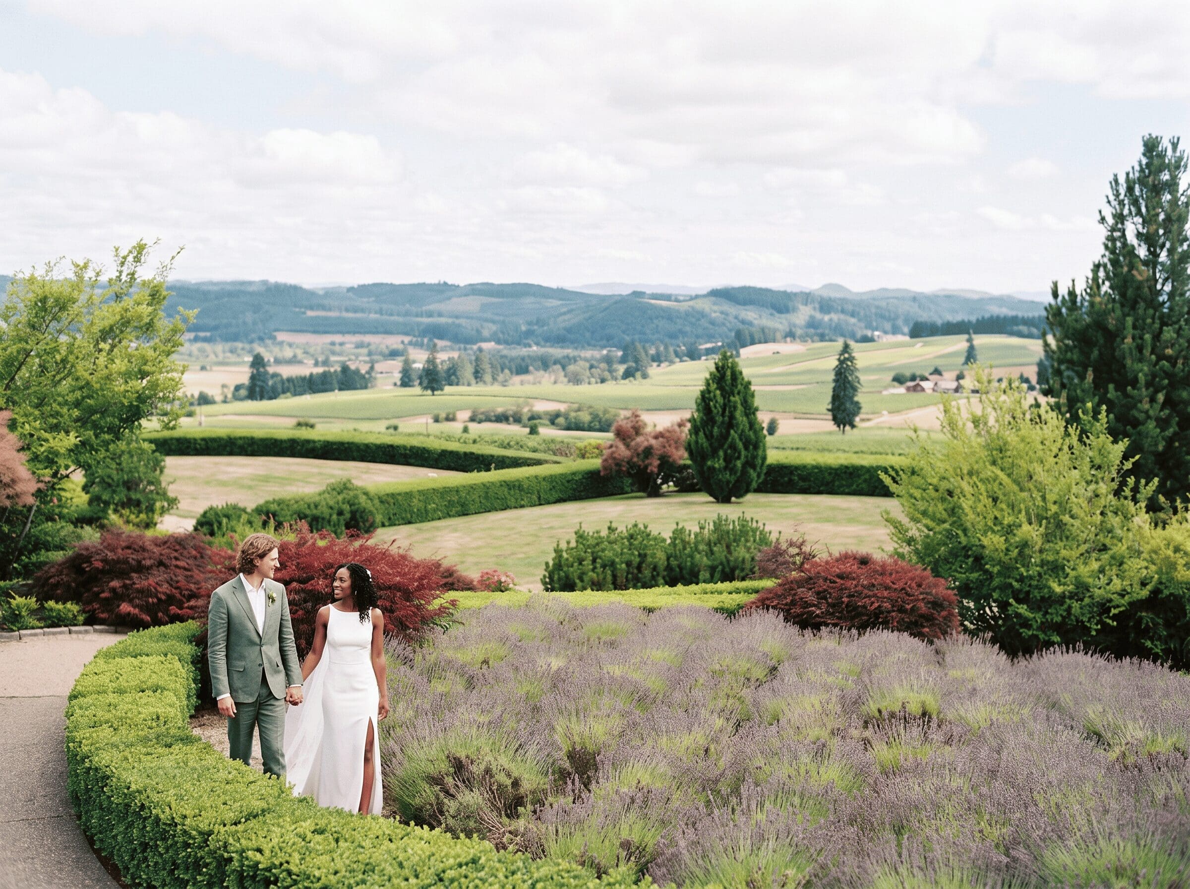 King Estate wedding couple holding hands along the lavender garden path, with panoramic vineyard and farmland views just outside Eugene in the Southern Willamette Valley.