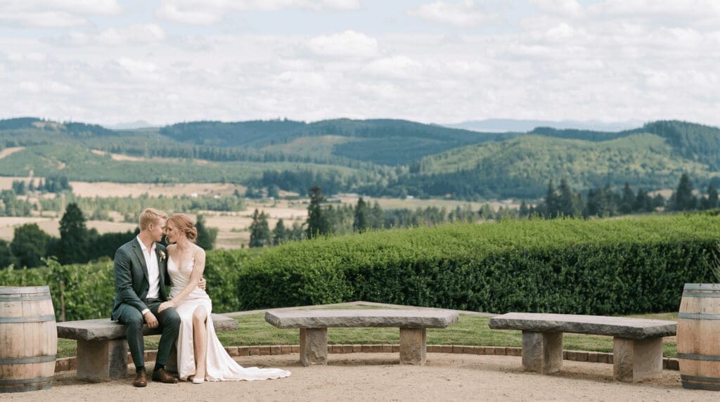 Newlyweds sitting on a stone bench at King Estate, overlooking vineyard rows and the Southern Willamette Valley hills during their intimate micro wedding celebration.