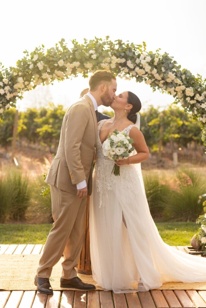 Newlyweds kiss beneath a lush floral arch at an outdoor ceremony, highlighting how an Oregon Coast day-of coordinator keeps the timeline, vendors, and ceremony details running smoothly.
