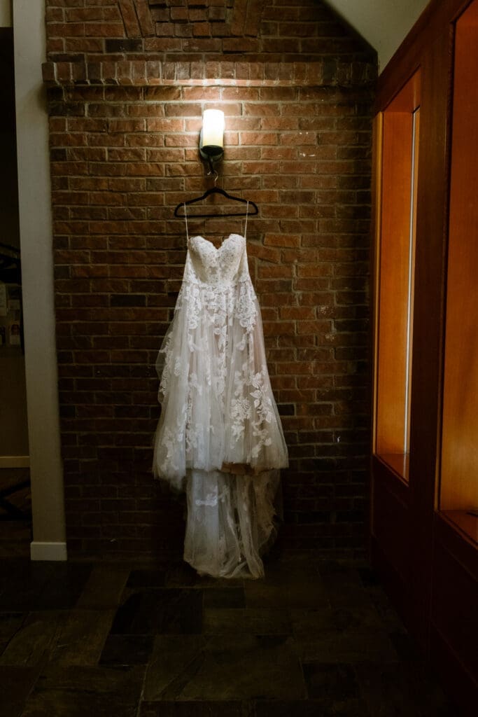 Lace wedding gown hanging on an exposed brick wall in the bridal suite at The Foundry in Lake Oswego