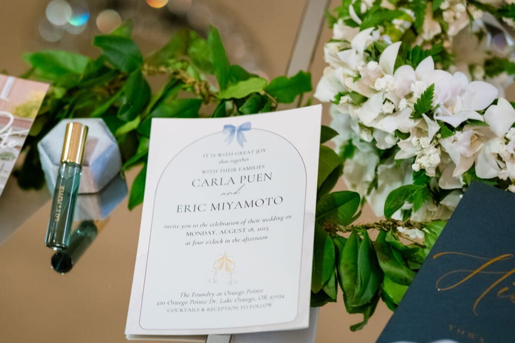 Carla and Eric's wedding invitation resting beside white florals at their Lake Oswego wedding