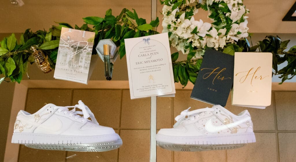 Wedding detail flat lay with Carla and Eric's invitation, vow books, and matching white Nike sneakers at The Foundry