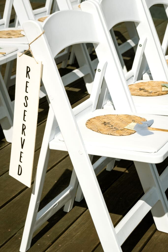 White ceremony chairs with a reserved sign and woven fans for guests at The Foundry in Lake Oswego