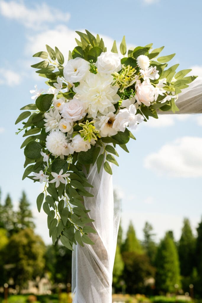 Close-up of the white and blush arbor florals against the sky at a Lake Oswego wedding ceremony