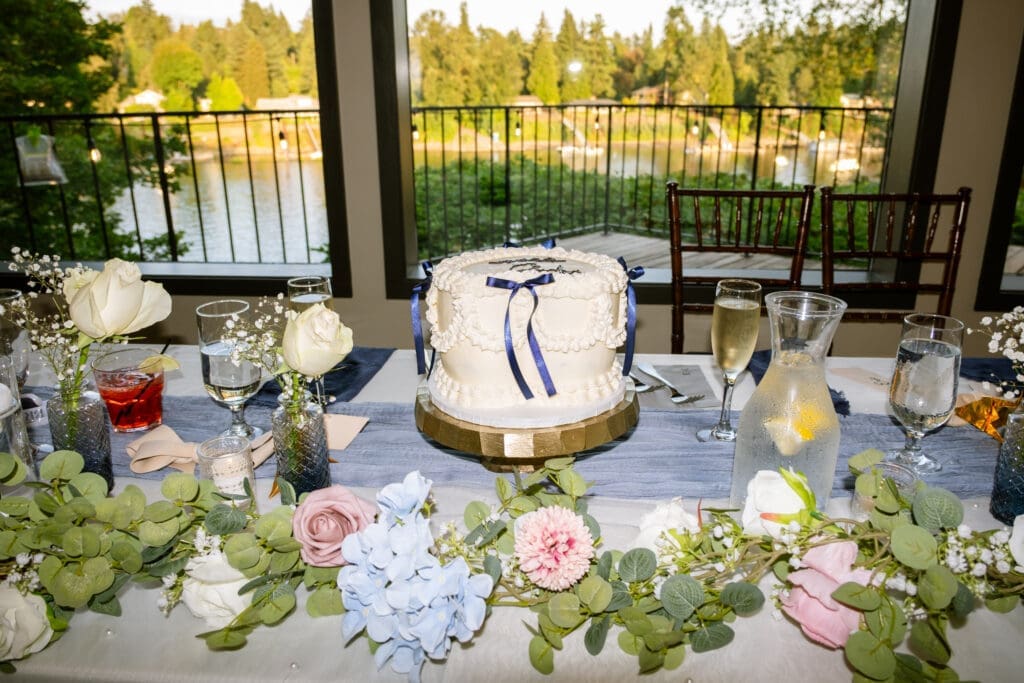 Sweetheart table with the wedding cake and blue and white floral garland overlooking the river at a Portland intimate wedding